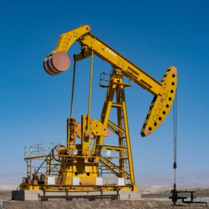 A yellow oil pump jack operating on an open field against a clear blue sky.